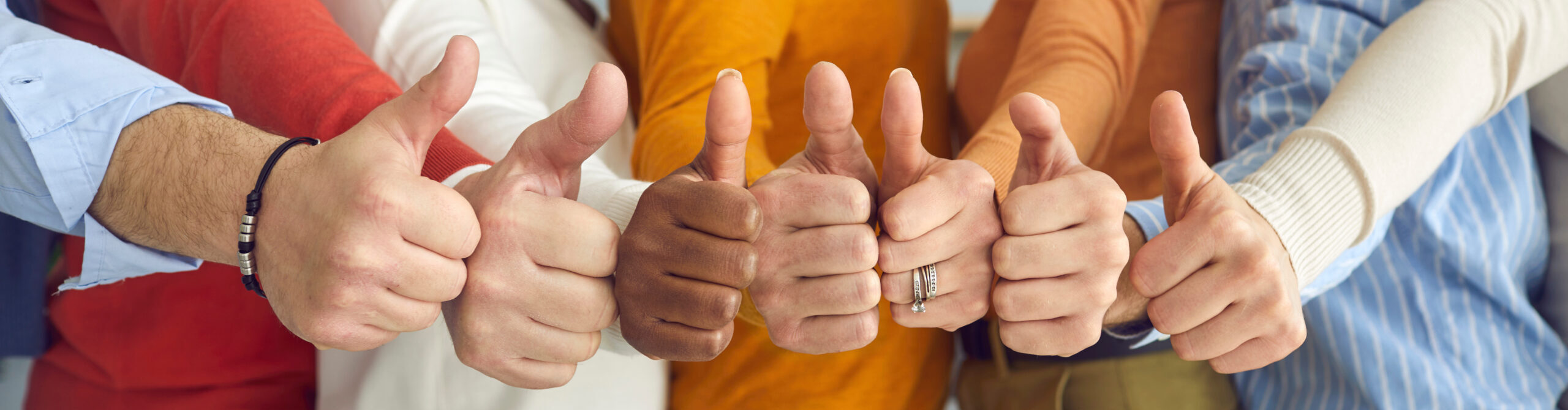 Hymyilevä ja monimuotoinen tiimi tyytyväisenä onnistuneeseen tiimityöhön näyttää peukkua